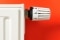 A radiator against a red wall with the thermostatic radiator valve pointing to number three